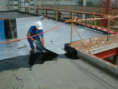 Operario con casco extiende Polibreal con llana sobre una cubierta, junto a una lámina de aluminio y cinta de obra