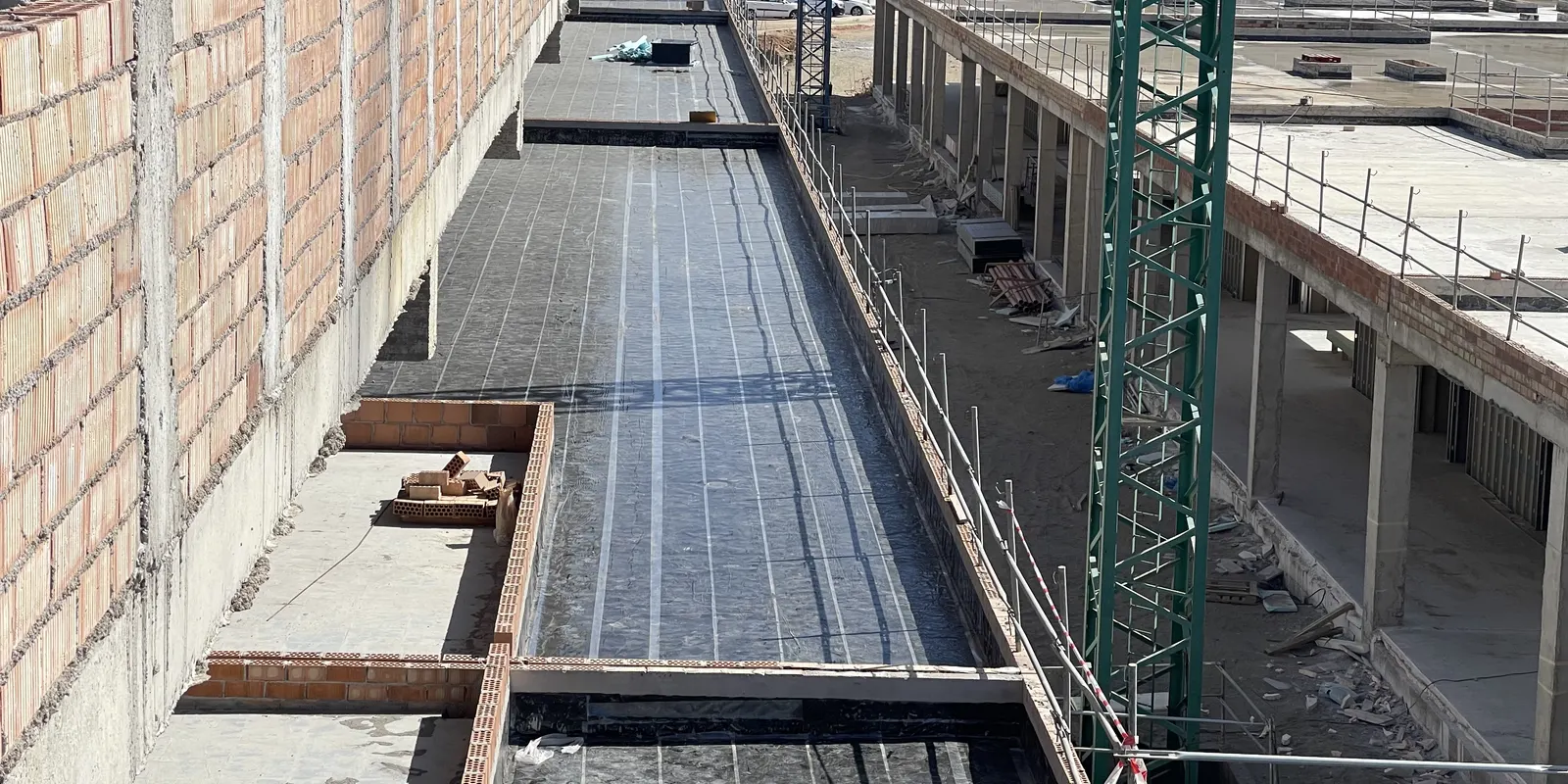 Terraza en obra con la membrana impermeabilizante extendida entre muros de ladrillo y una grúa al fondo