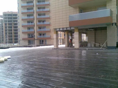 Plaza sobre forjado cubierta con membrana negra brillante, rodeada de edificios de viviendas de fachada clara