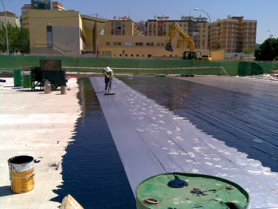 Operario con llana aplica Polibreal sobre una lámina de aluminio en una cubierta amplia, con bidones delante