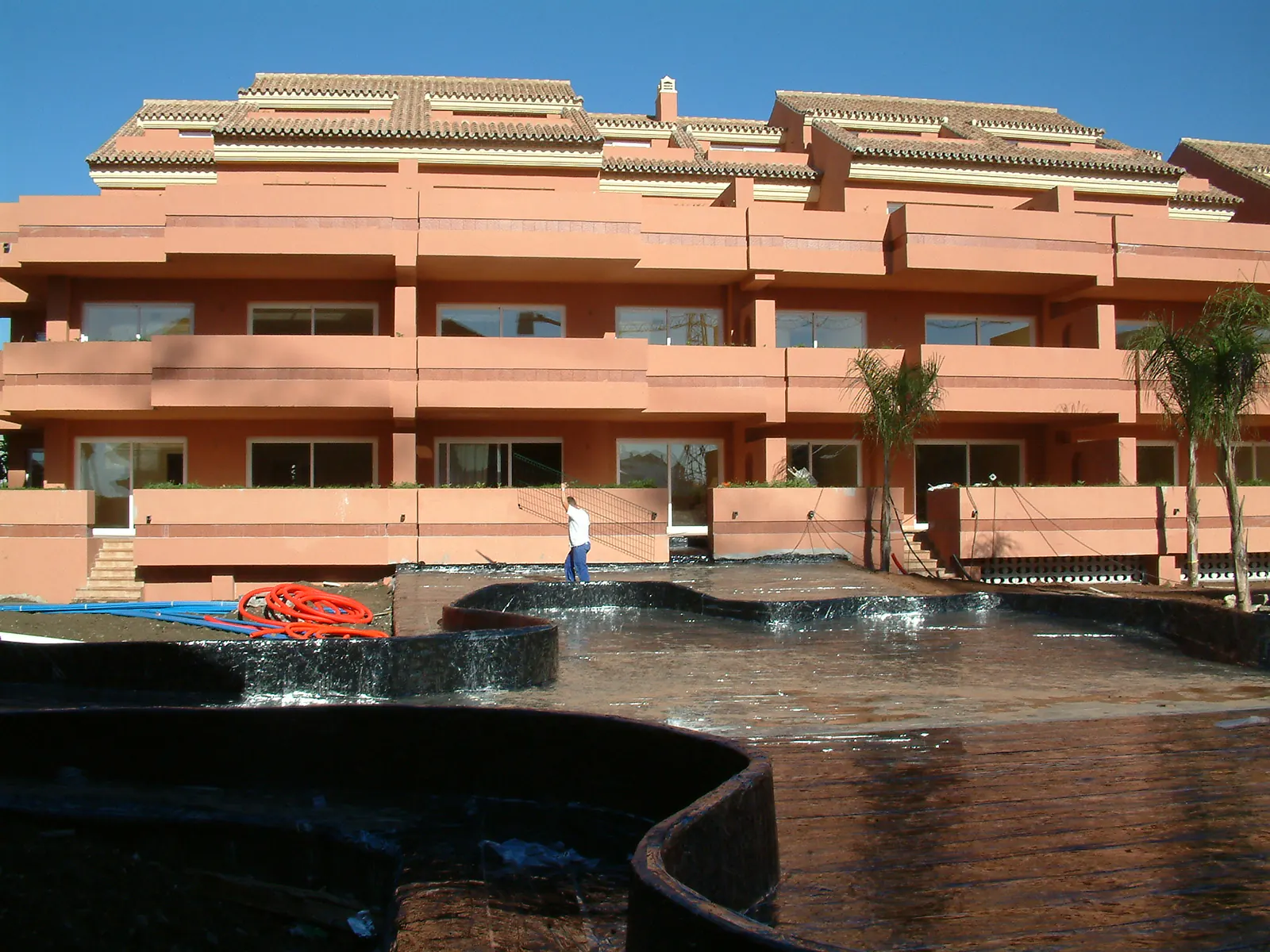Jardineras curvas impermeabilizadas y cubiertas de agua frente a un edificio residencial de color terracota