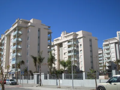Bloques de apartamentos de color crema con terrazas y palmeras delante, bajo un cielo azul