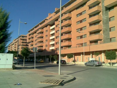 Largo bloque de viviendas de fachada anaranjada con terrazas, junto a una calle con farolas y árboles