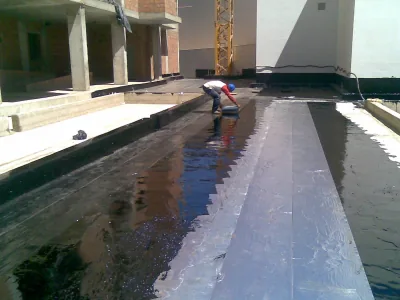 Operario agachado extiende Polibreal negro sobre un forjado, junto a una franja de lámina de aluminio