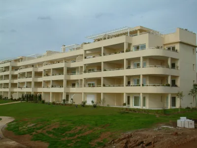 Edificio residencial escalonado de color crema con amplias terrazas y césped delante, bajo un cielo nublado