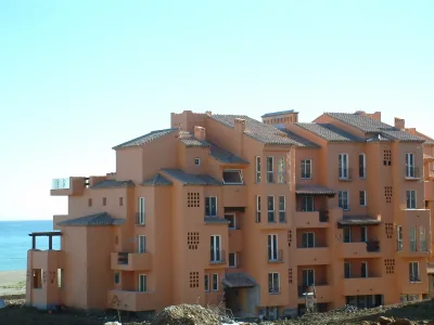 Edificio residencial de color salmón con tejados de teja y el mar al fondo a la izquierda