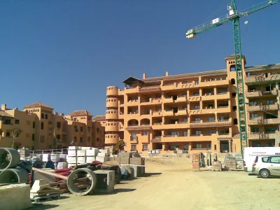Edificios residenciales de color terracota en construcción, con grúa torre y materiales de obra delante