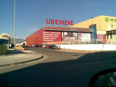 Fachada roja de una tienda de electrodomésticos Urende junto a una calle, vista desde dentro de un coche
