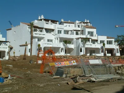 Viviendas blancas de estilo andaluz con tejas y palmeras, con vallas de obra y señales de seguridad delante